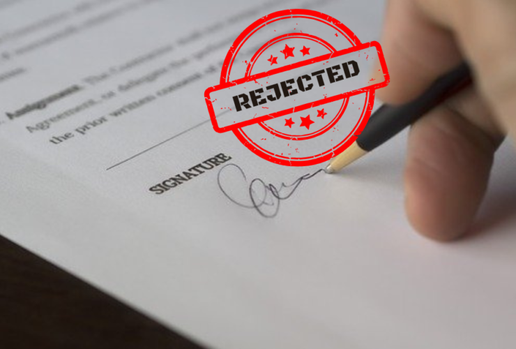 A hand signing a document with a stamp saying "rejected"